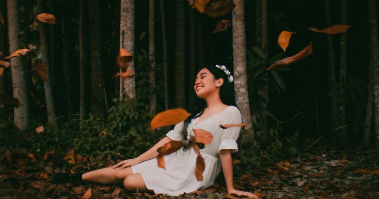 Woman in white dress smiling in forest.