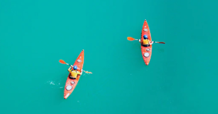 Two red kayaks with people paddling on turquoise water.