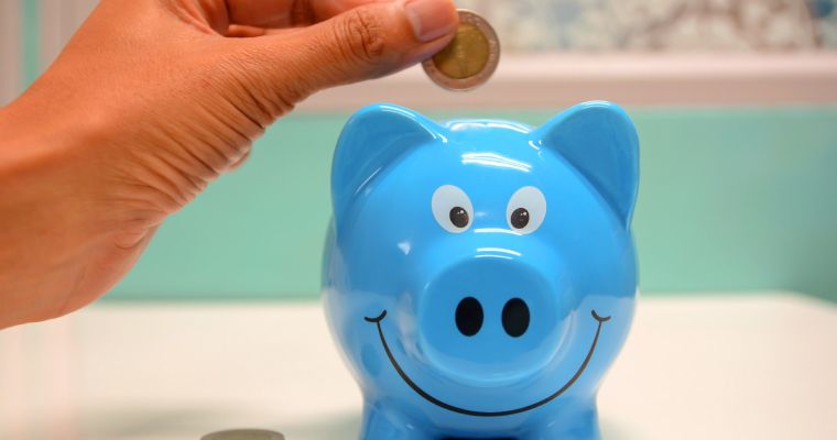 Hand putting coin in blue piggy bank.