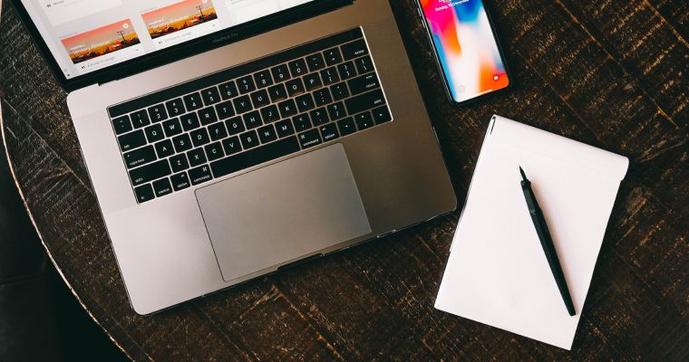 Laptop, phone, pen, and notebook on a table.