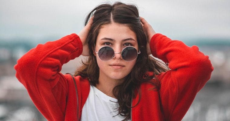 Woman in red jacket wearing round sunglasses.